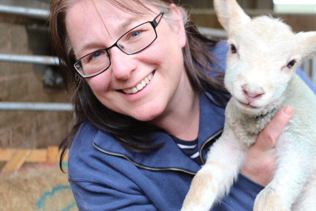 Liz smiling and holding a live lamb